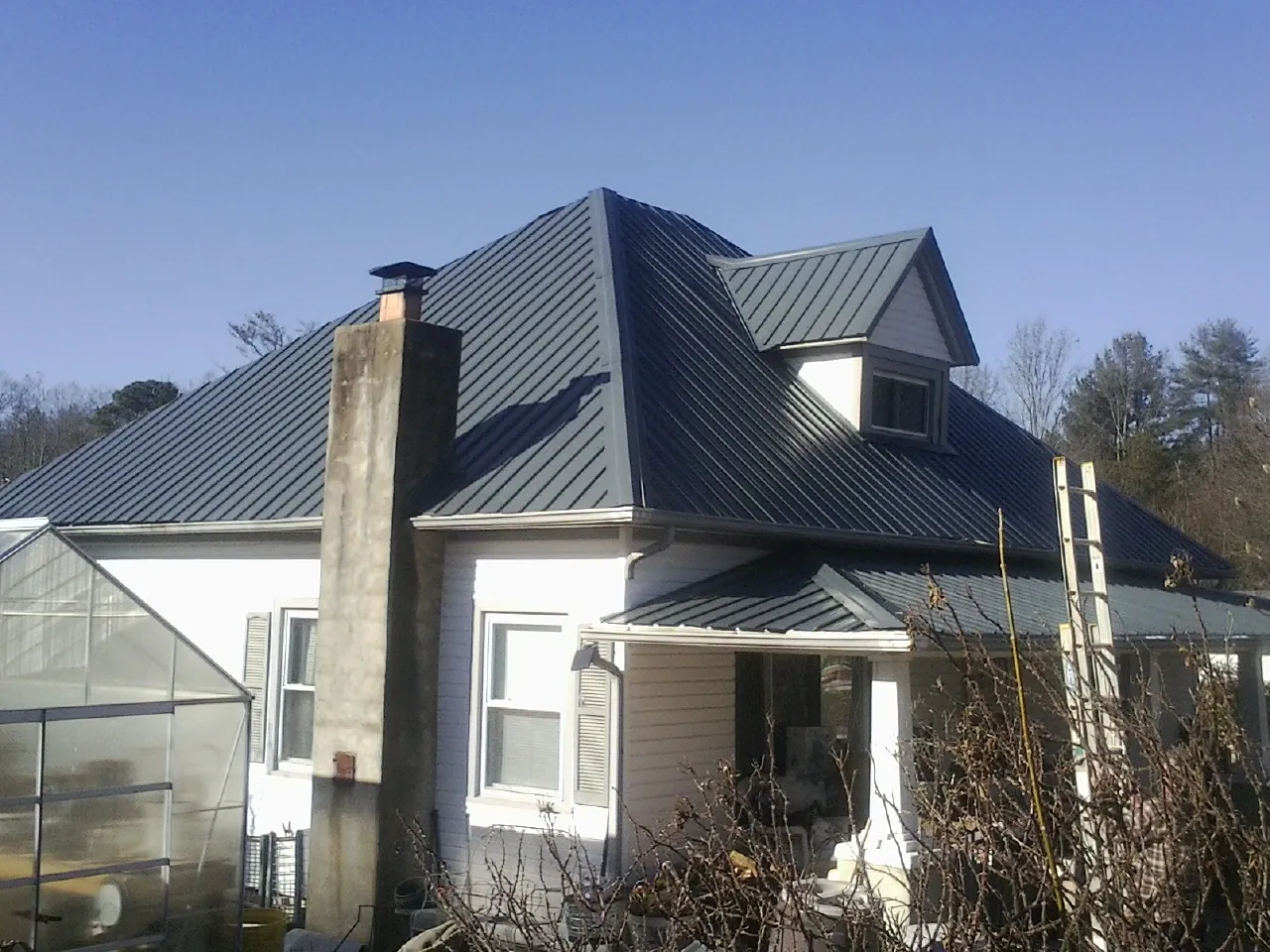 Dark blue standing seam metal roof on a white farmhouse with dormer — Slate & Tile Roof Repair by Roofing Brothers in Hubbardston