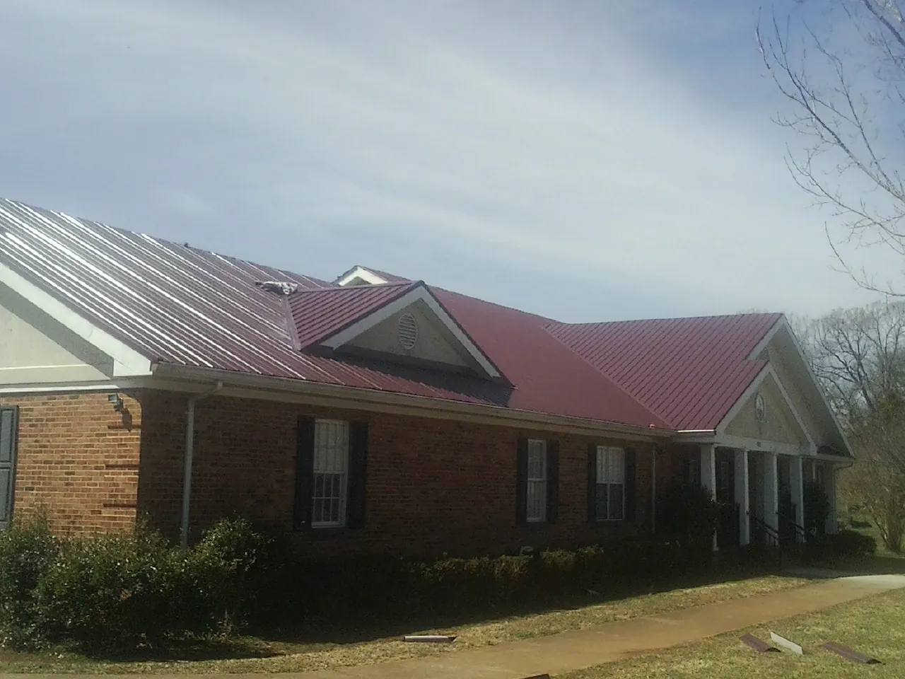 Red metal roof with gabled entries on a long brick building, from a Hail Damage Roof Repair job in Hubbardston