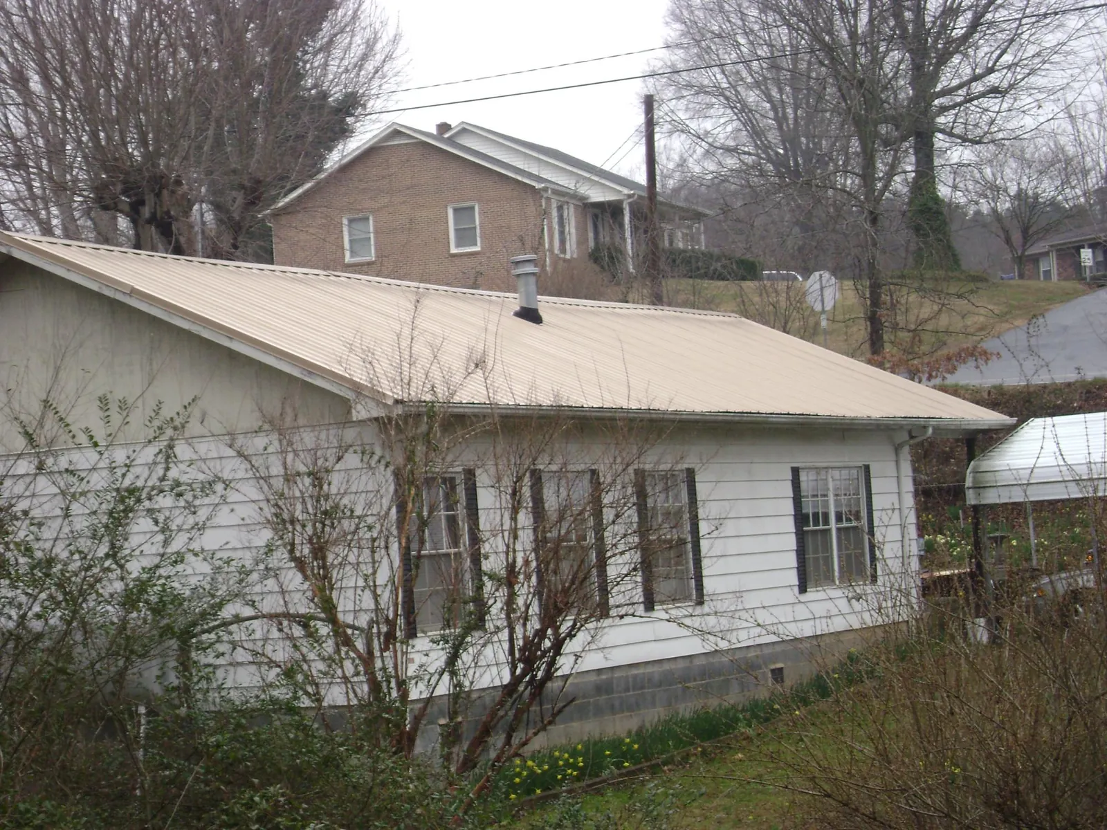 Tan metal roof on a white sided house set into a hillside — Commercial Roofing by Roofing Brothers in Hubbardston