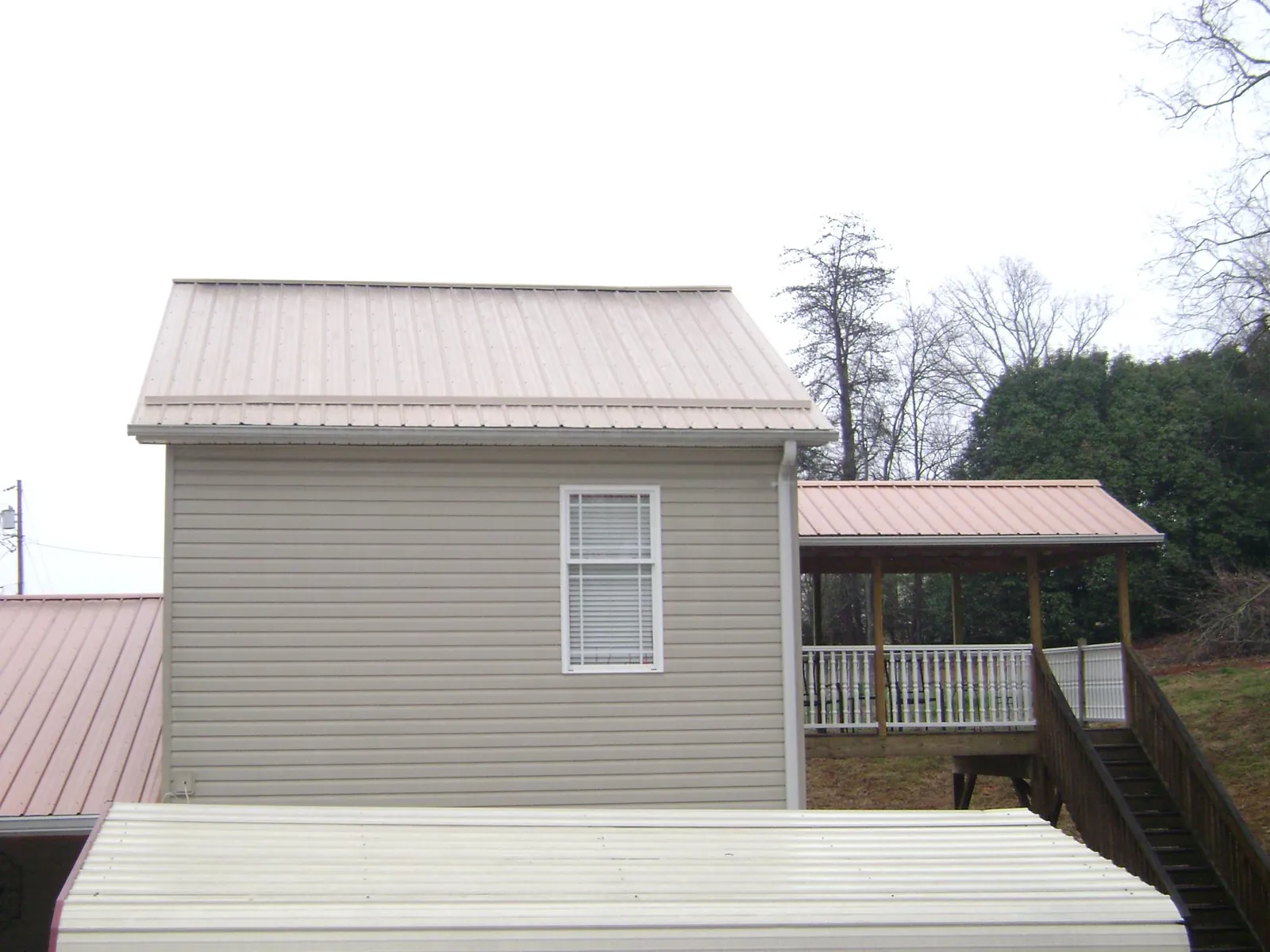 Tan metal roofs on a two story addition and attached porch, from a Roof Replacement job in Hubbardston